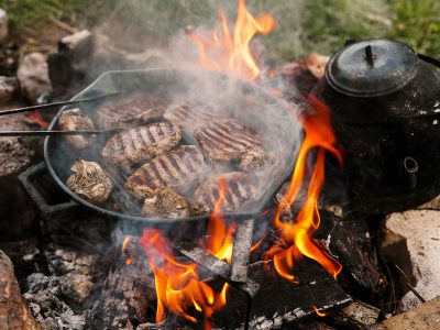 Campfire red meat in pan, near the fire outdoors. bushcraft, adventure, tea, knife and camping concept